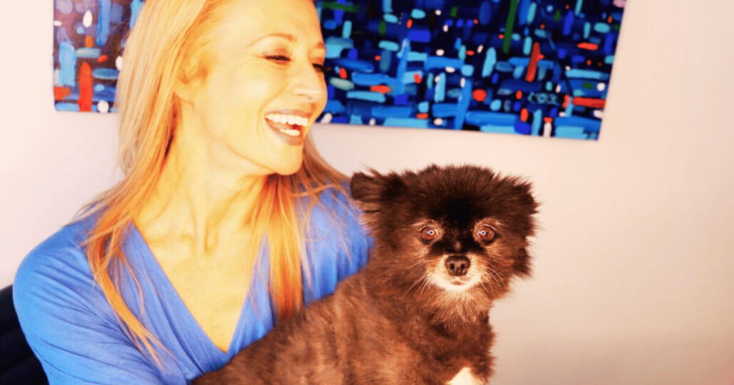 Dr. Madisen Harper with Pomeranian dog, Minka, smiles in front of abstract art as they work from home.